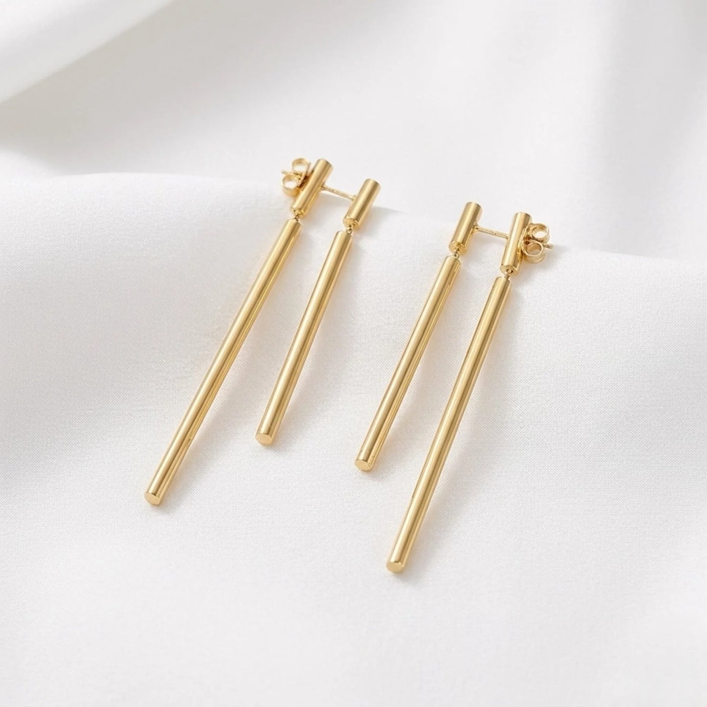 BEHI MILANO Deffi Earrings — pair of gold double cylinder drop earrings on draped white silk