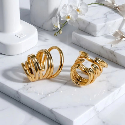 BEHI MILANO Denyse Ear Cuffs — pair of gold multi-wrap spiral ear cuffs on white marble display