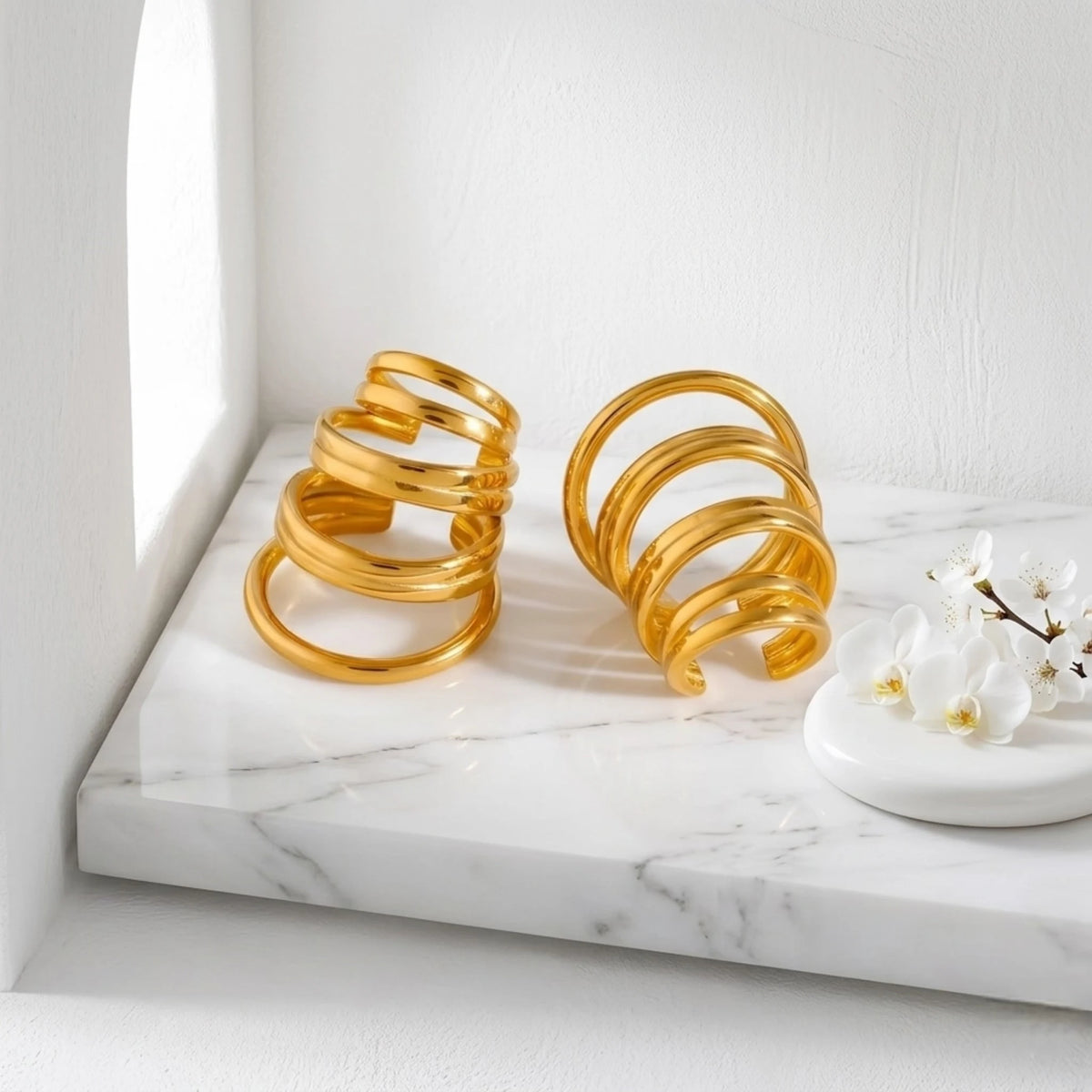 BEHI MILANO Denyse Ear Cuffs — gold spiral non-pierced ear cuffs displayed on marble pedestal