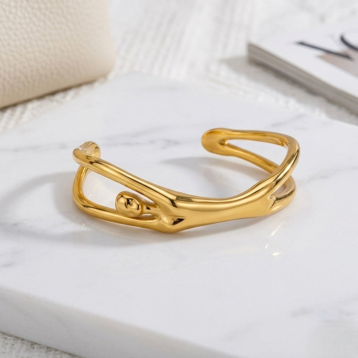 BEHI MILANO Devika Bracelet — top view of gold sculptural body shape cuff on marble slab