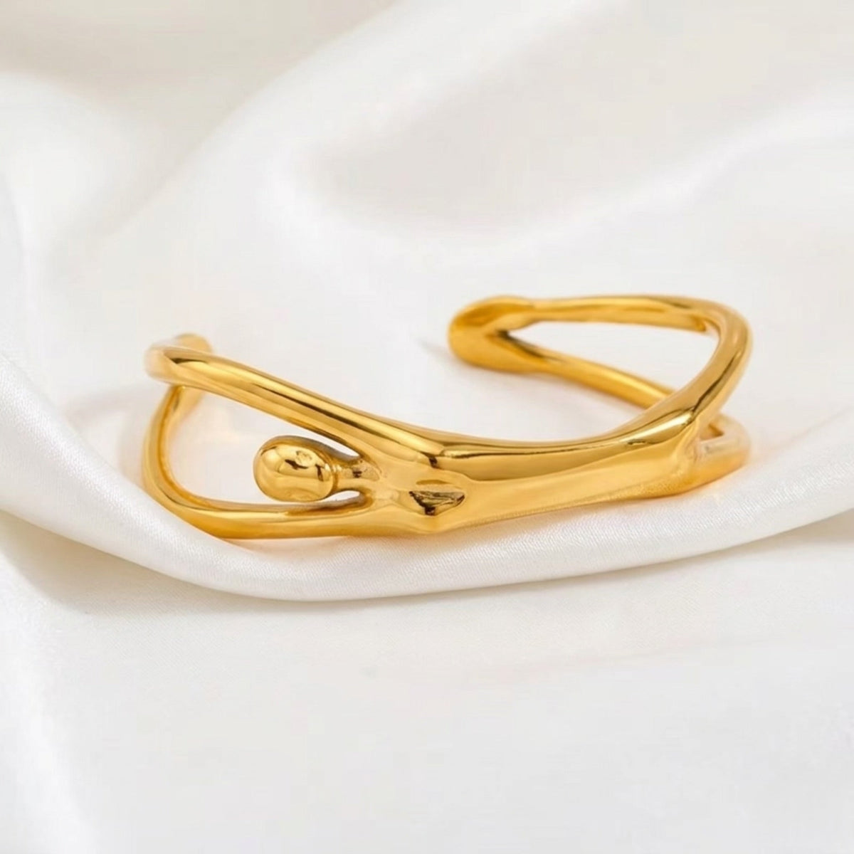 BEHI MILANO Devika Bracelet — gold abstract cuff standing on draped white silk cloth