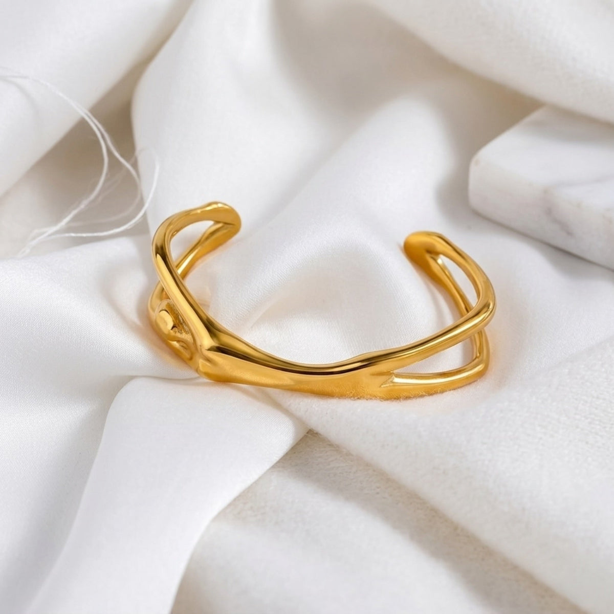 BEHI MILANO Devika Bracelet — 18k gold open-cuff bracelet lying on white silk drapery