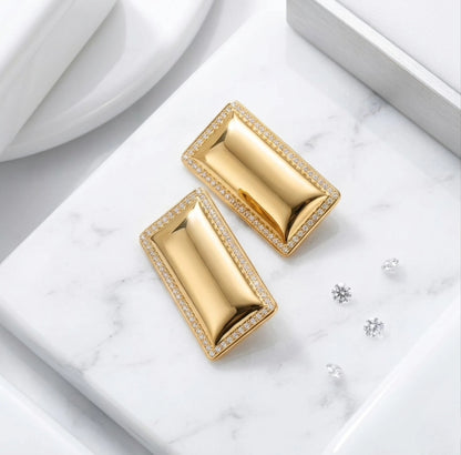 BEHI MILANO Dezi Earrings — gold rectangular studs on white marble slab surrounded by micro crystals