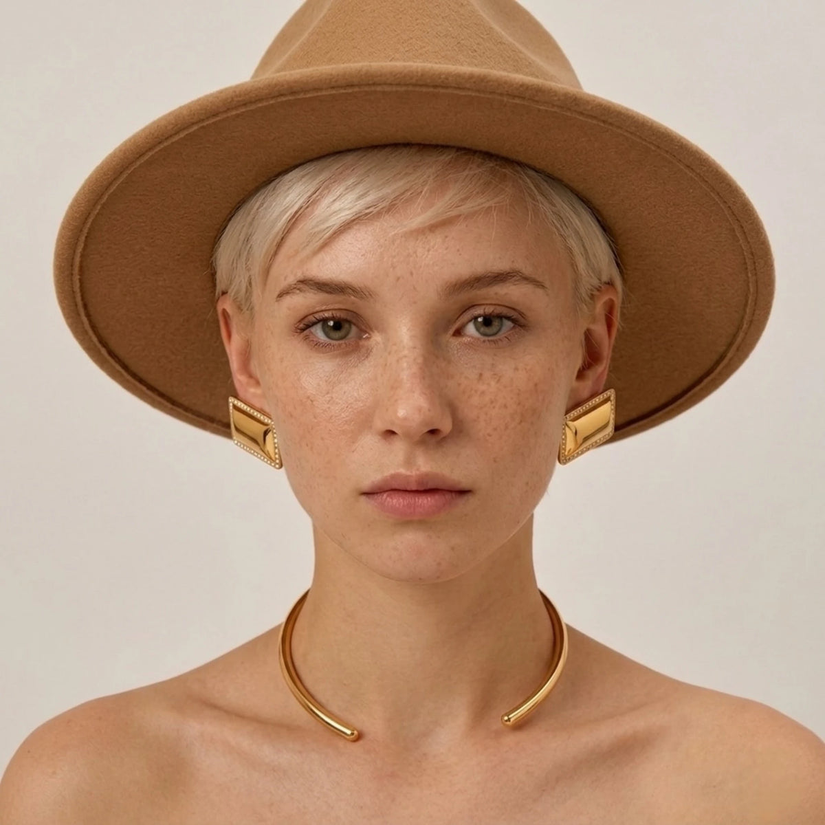 BEHI MILANO Dezi Earrings — model front portrait wearing gold rectangular statement studs and hat