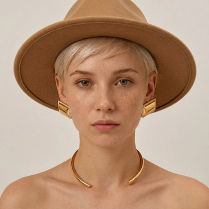 BEHI MILANO Dezi Earrings — model front portrait wearing gold rectangular statement studs and hat