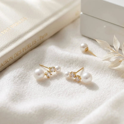 BEHI MILANO Diana Earrings — gold pearl and zircon stud earrings resting on white silk fabric