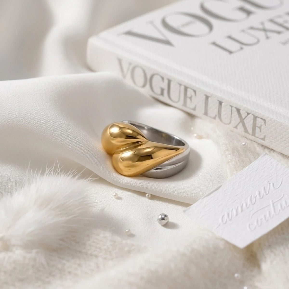 BEHI MILANO Disha Ring — gold and silver sculptural ring resting on white silk with Vogue Luxe book
