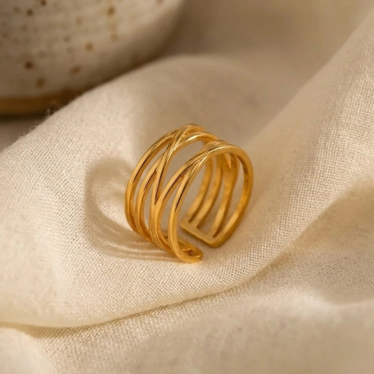 BEHI MILANO Eden Ring — gold wide band ring resting on soft beige silk fabric