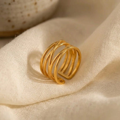 BEHI MILANO Eden Ring — gold wide band ring resting on soft beige silk fabric