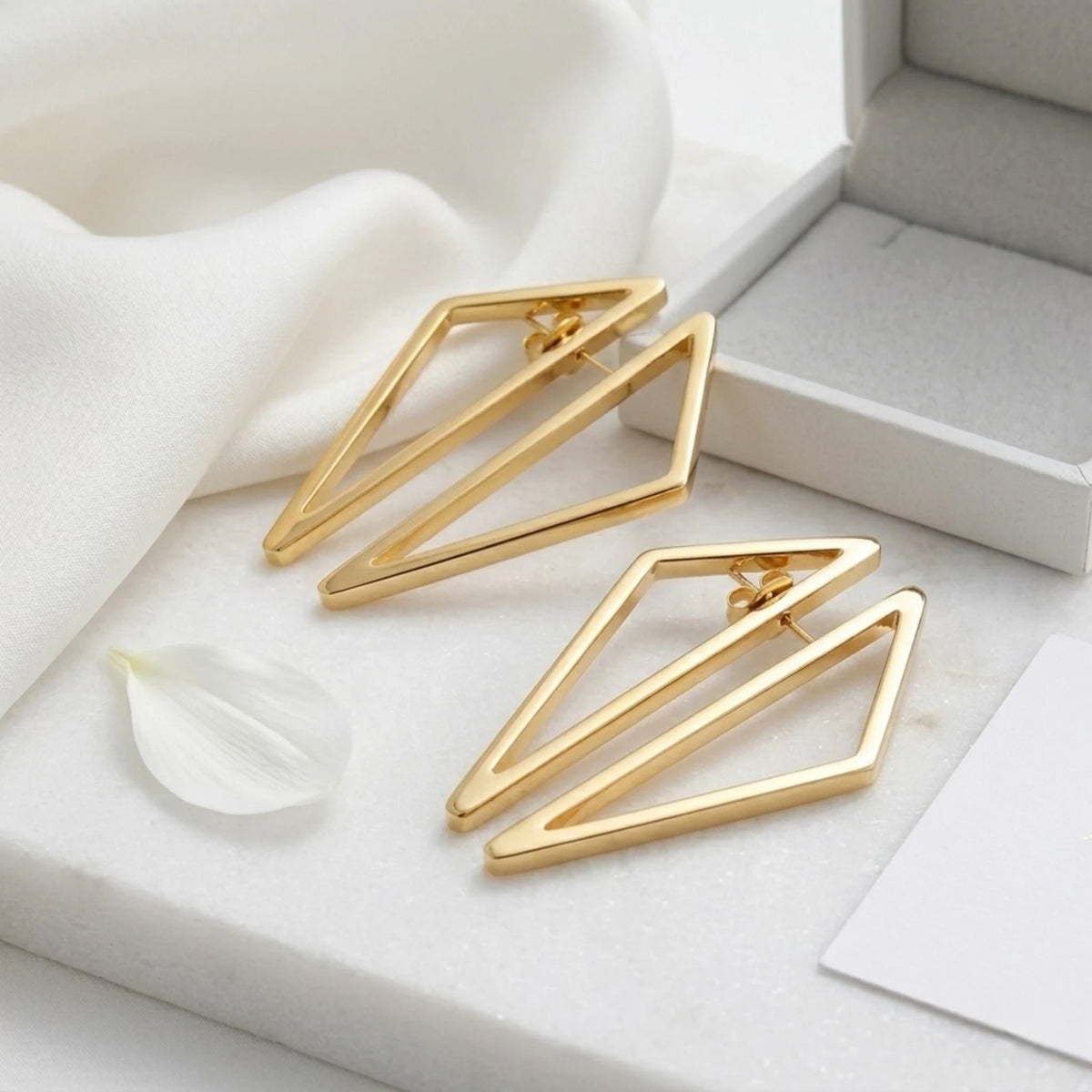 BEHI MILANO Elif Earrings — pair of gold architectural earrings resting on soft white cloth