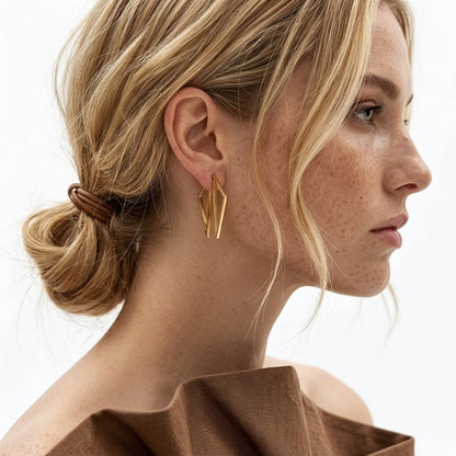 BEHI MILANO Elif Earrings — model wearing gold geometric polygonal earrings with low bun hairstyle