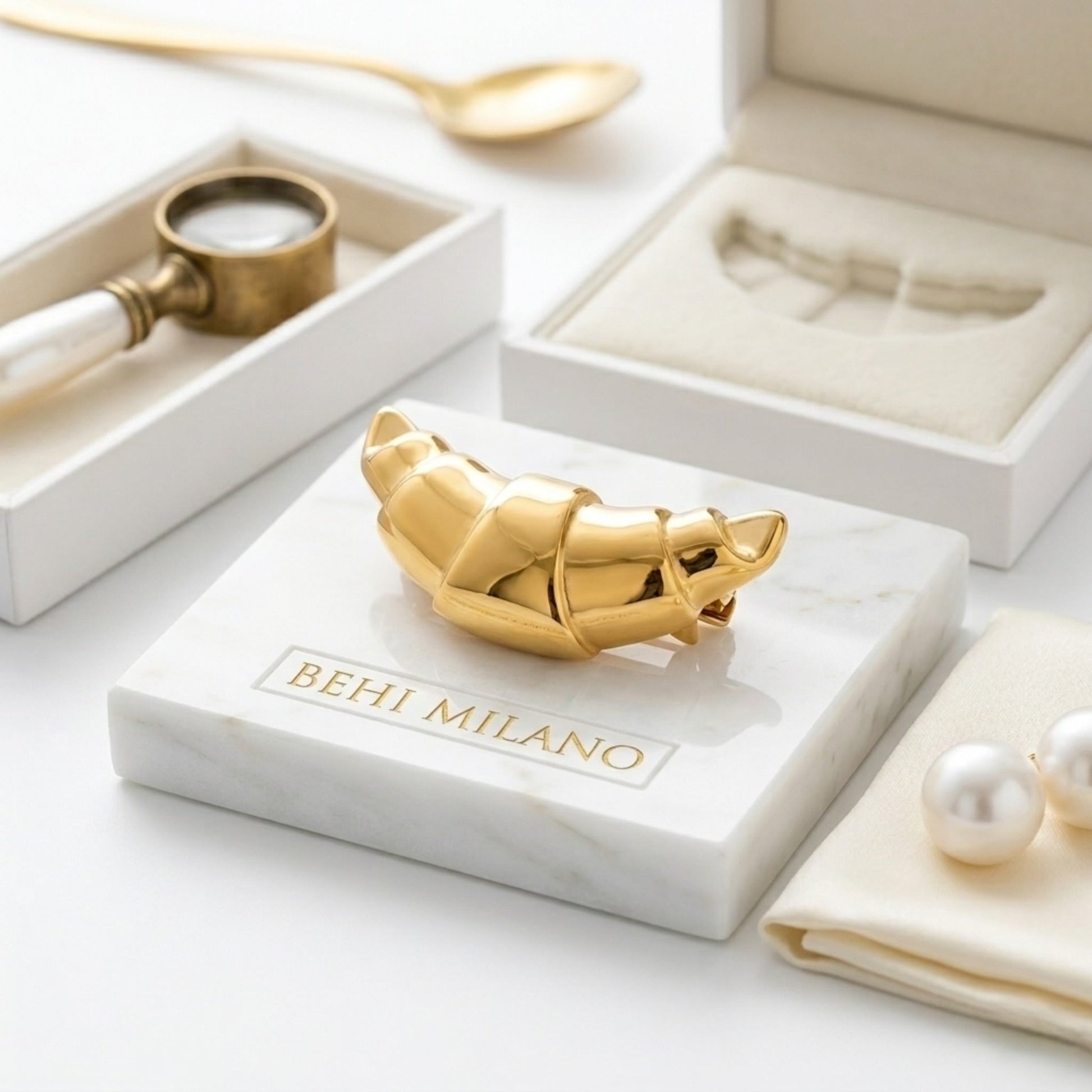 BEHI MILANO Elisa Brooch — gold croissant brooch displayed on white marble stone base