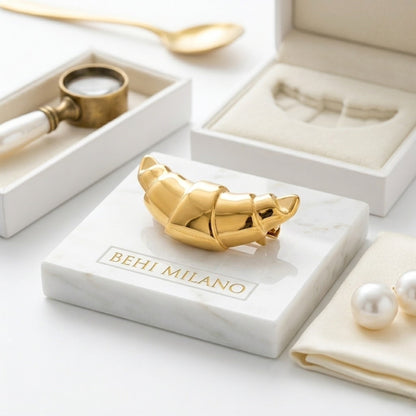 BEHI MILANO Elisa Brooch — gold croissant brooch displayed on white marble stone base