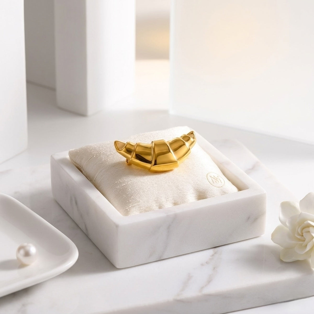 BEHI MILANO Elisa Brooch — gold croissant pin resting on white velvet jewelry cushion
