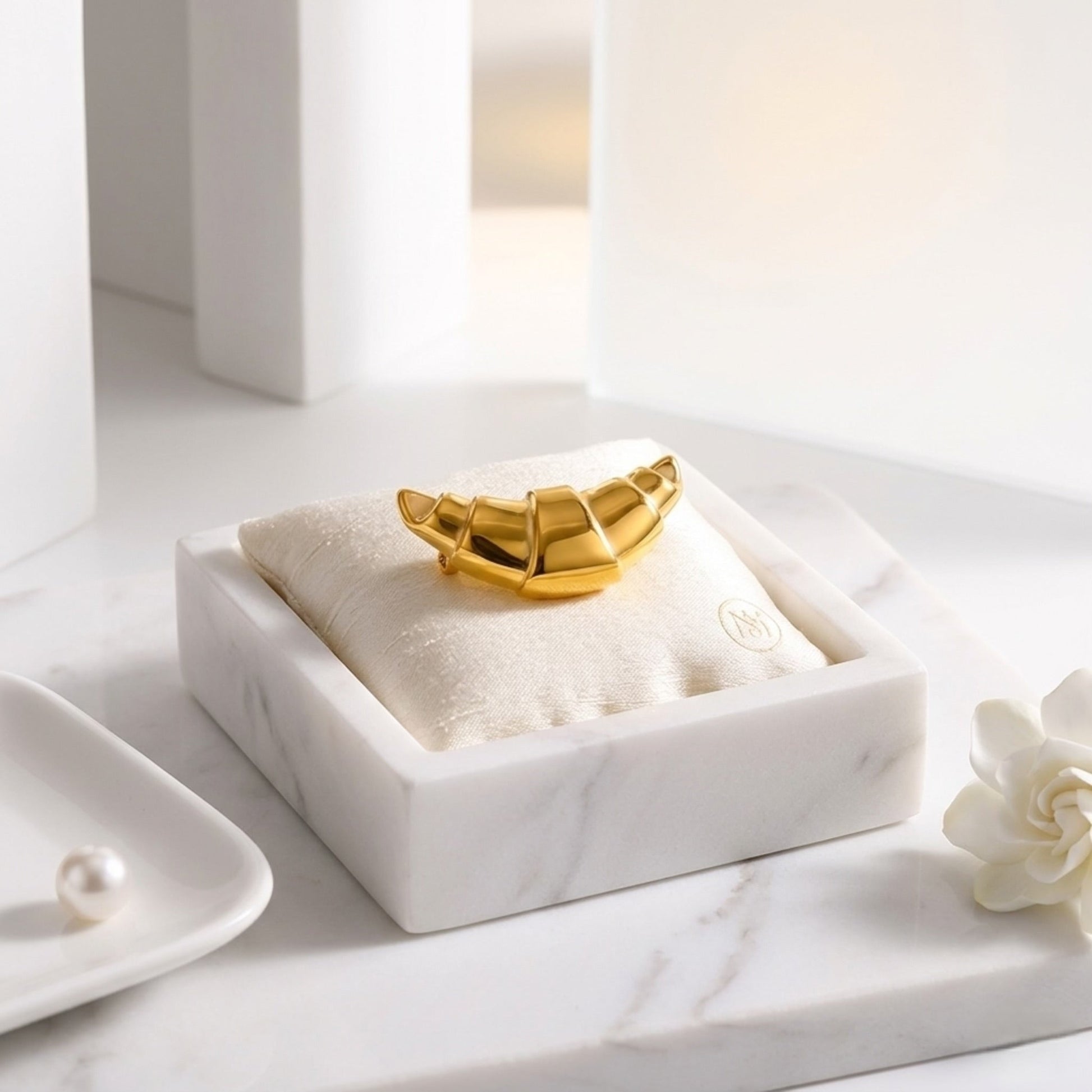 BEHI MILANO Elisa Brooch — gold croissant pin resting on white velvet jewelry cushion