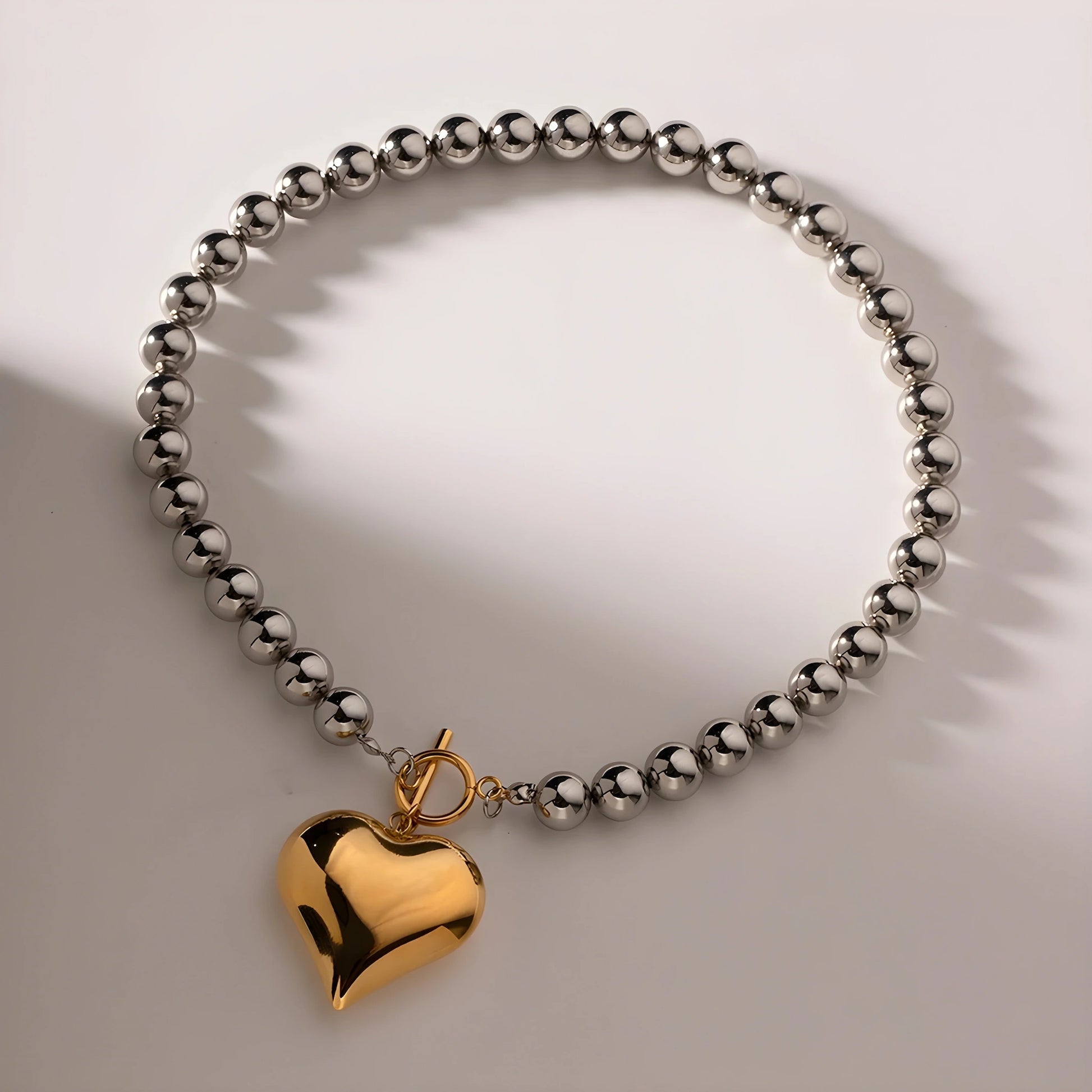 BEHI MILANO Emma Choker — gold heart charm and silver bead necklace with soft shadow lighting