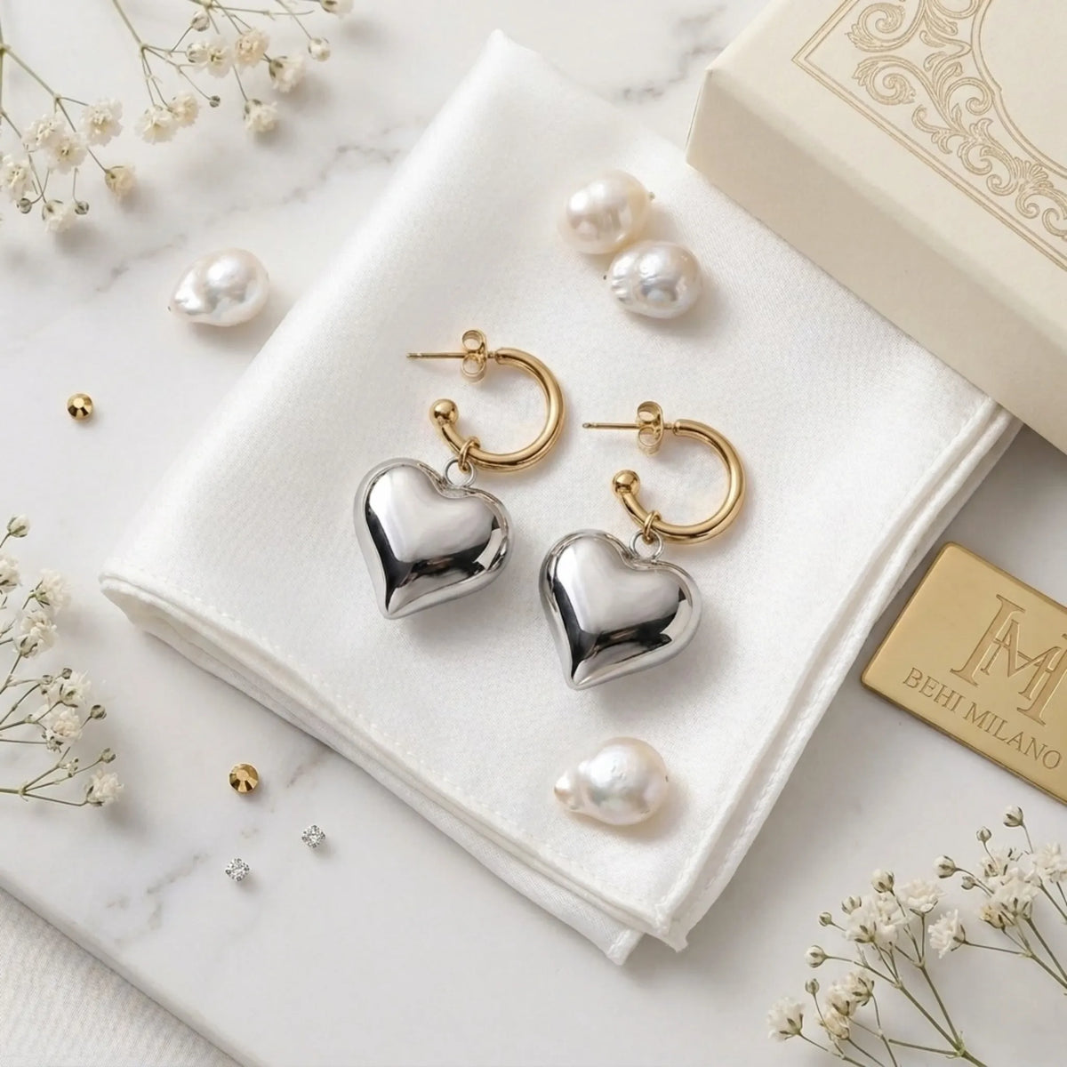 BEHI MILANO Emma Earrings — gold and silver puffy heart drop earrings on white fabric