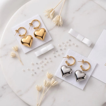 BEHI MILANO Emma Earrings — gold and silver heart drop hoops displayed on marble with dried flowers