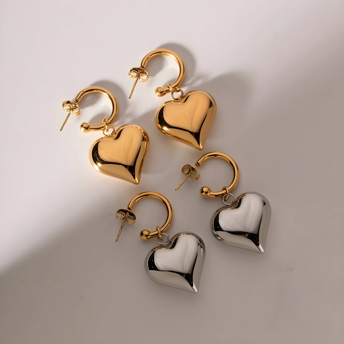 BEHI MILANO Emma Earrings — gold and silver heart hoop pairs under soft studio shadows