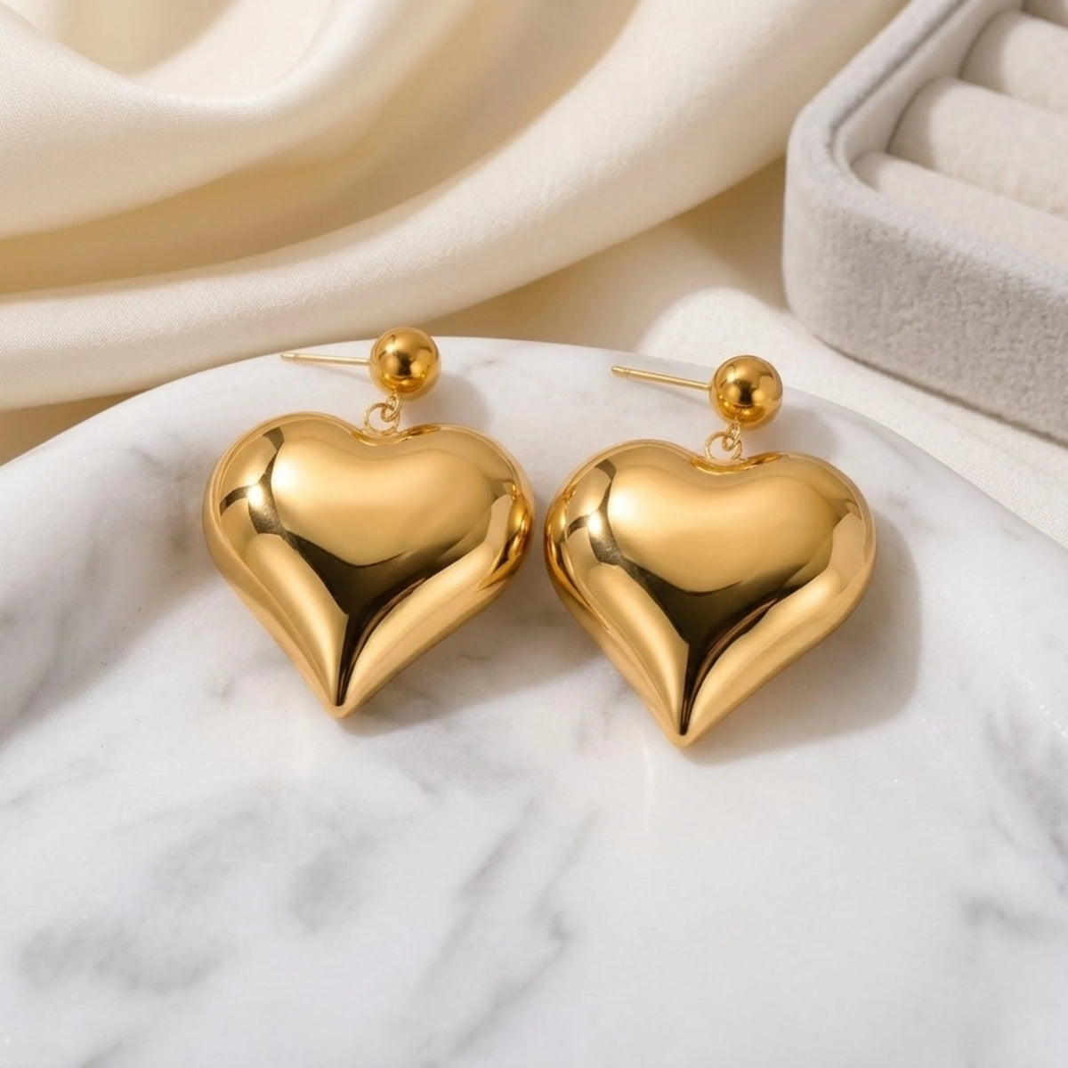 BEHI MILANO Emma XL Earrings — 18k gold oversized puffy heart drop earrings on white marble tray