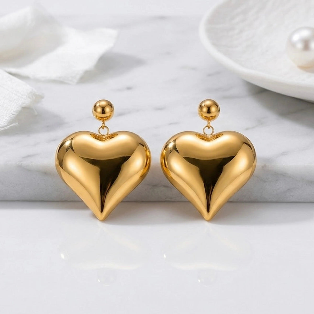 BEHI MILANO Emma XL Earrings — gold puffy heart statement drop earrings displayed on studio tray