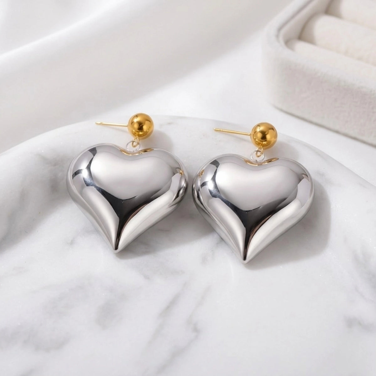 BEHI MILANO Emma XL Earrings — silver puffy heart earrings with gold studs displayed on white marble