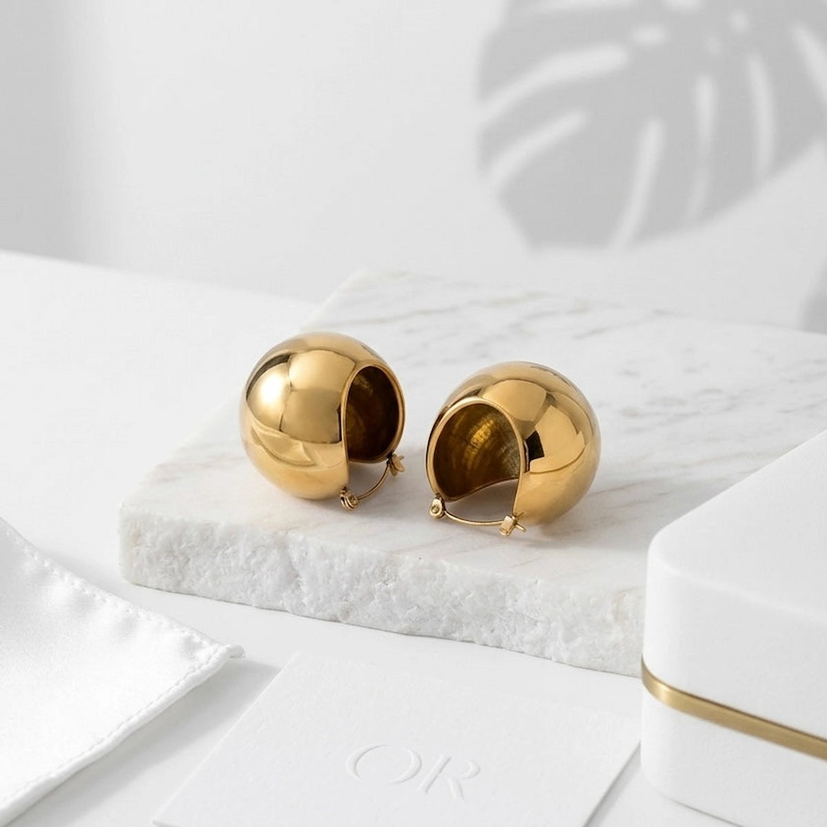 BEHI MILANO Erika Earrings — gold mirror-polished sphere earrings displayed on white marble