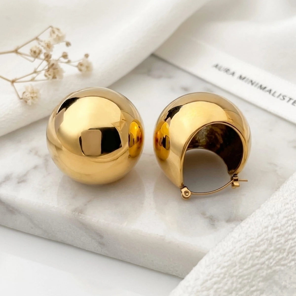 BEHI MILANO Erika Earrings — chunky gold spherical dome earrings on white marble display tray