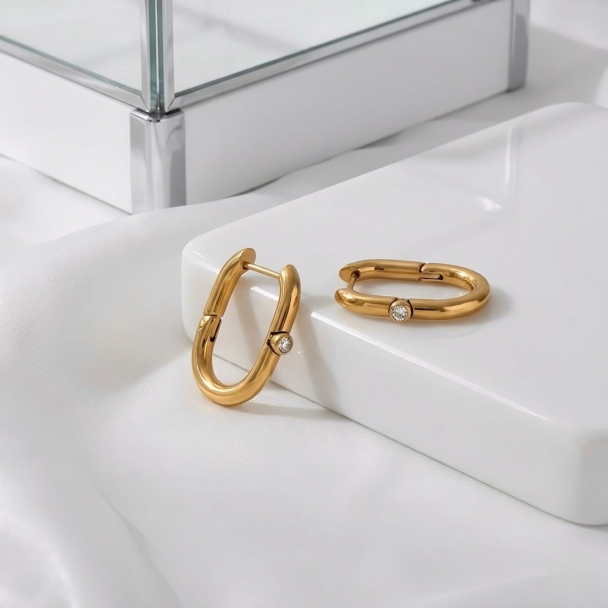 BEHI MILANO Eva Earrings — gold oval zircon hoop earrings close-up on white marble