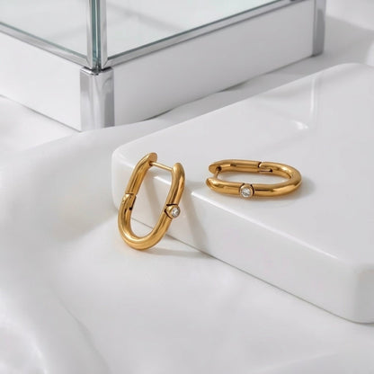 BEHI MILANO Eva Earrings — gold oval zircon hoop earrings close-up on white marble