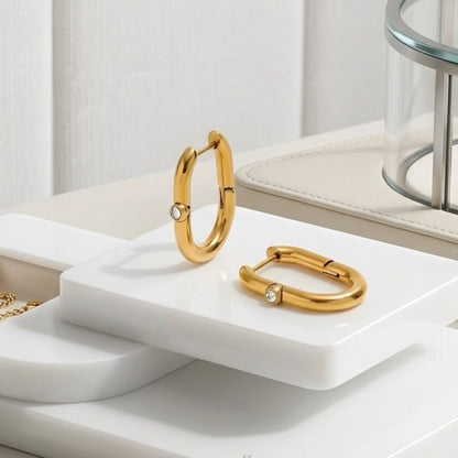 BEHI MILANO Eva Earrings — gold elongated oval hoop earrings displayed on white marble slab