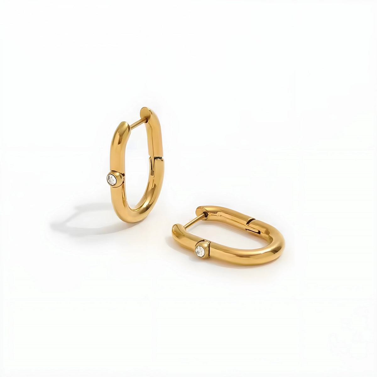 BEHI MILANO Eva Earrings — pair of gold oval huggie hoops standing on white surface