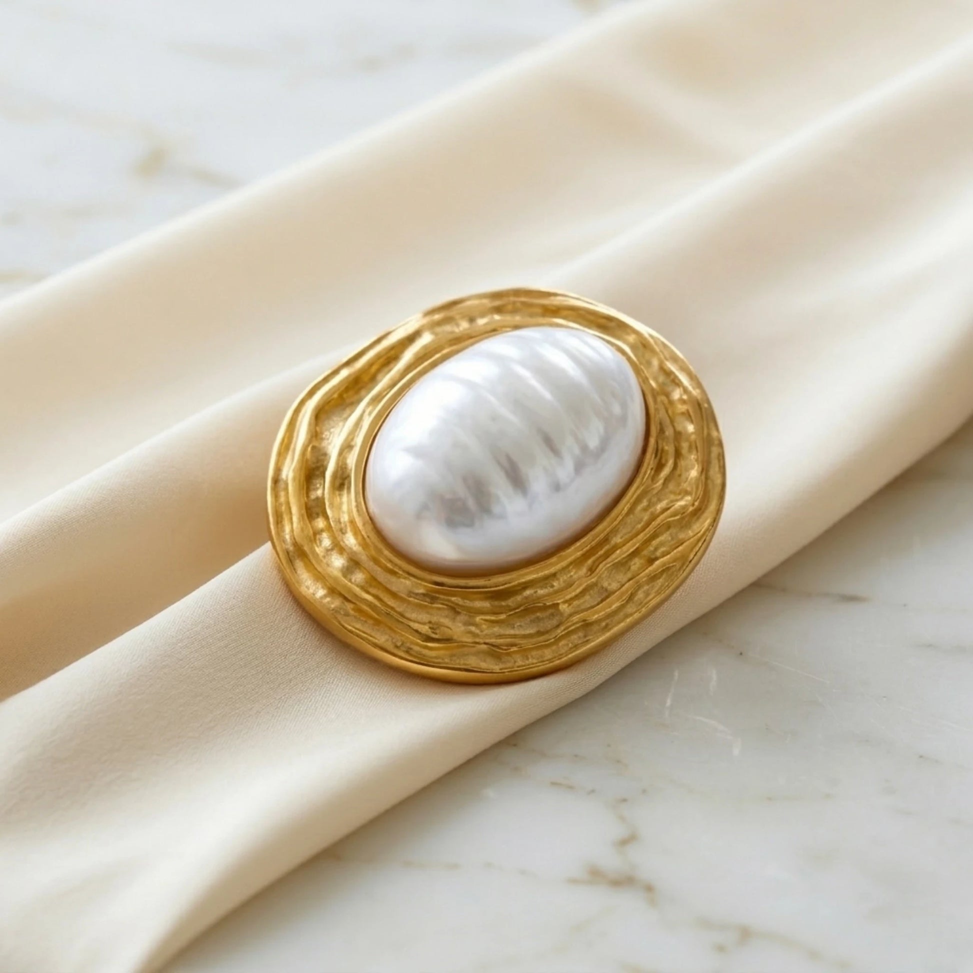 BEHI MILANO Everly Brooch — textured gold pearl brooch resting on cream silk fabric