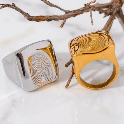 BEHI MILANO Fingerprint Ring — gold and silver square fingerprint rings displayed with decorative branch on marble