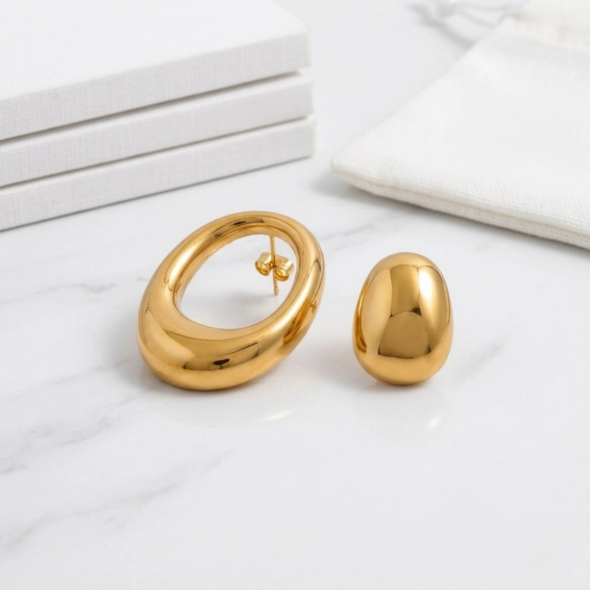 BEHI MILANO Fiona Earrings — gold asymmetric statement earrings flat lay on white marble