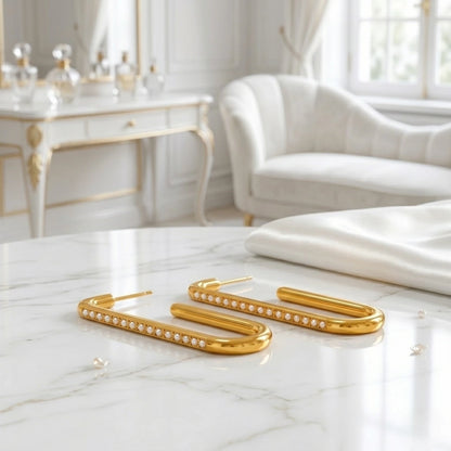 BEHI MILANO Floriana Earrings — gold pearl drop earrings displayed on marble table in elegant white room