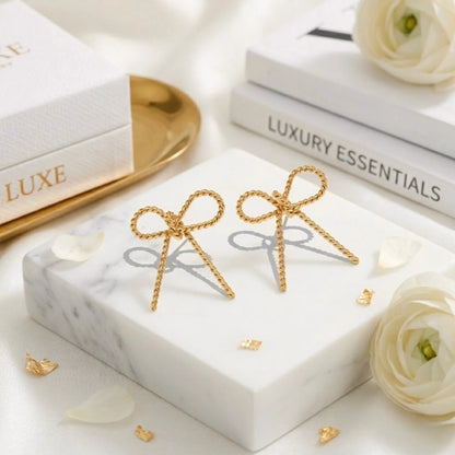 BEHI MILANO Francy Earrings — 18k gold twisted bow earrings displayed on white marble with flowers