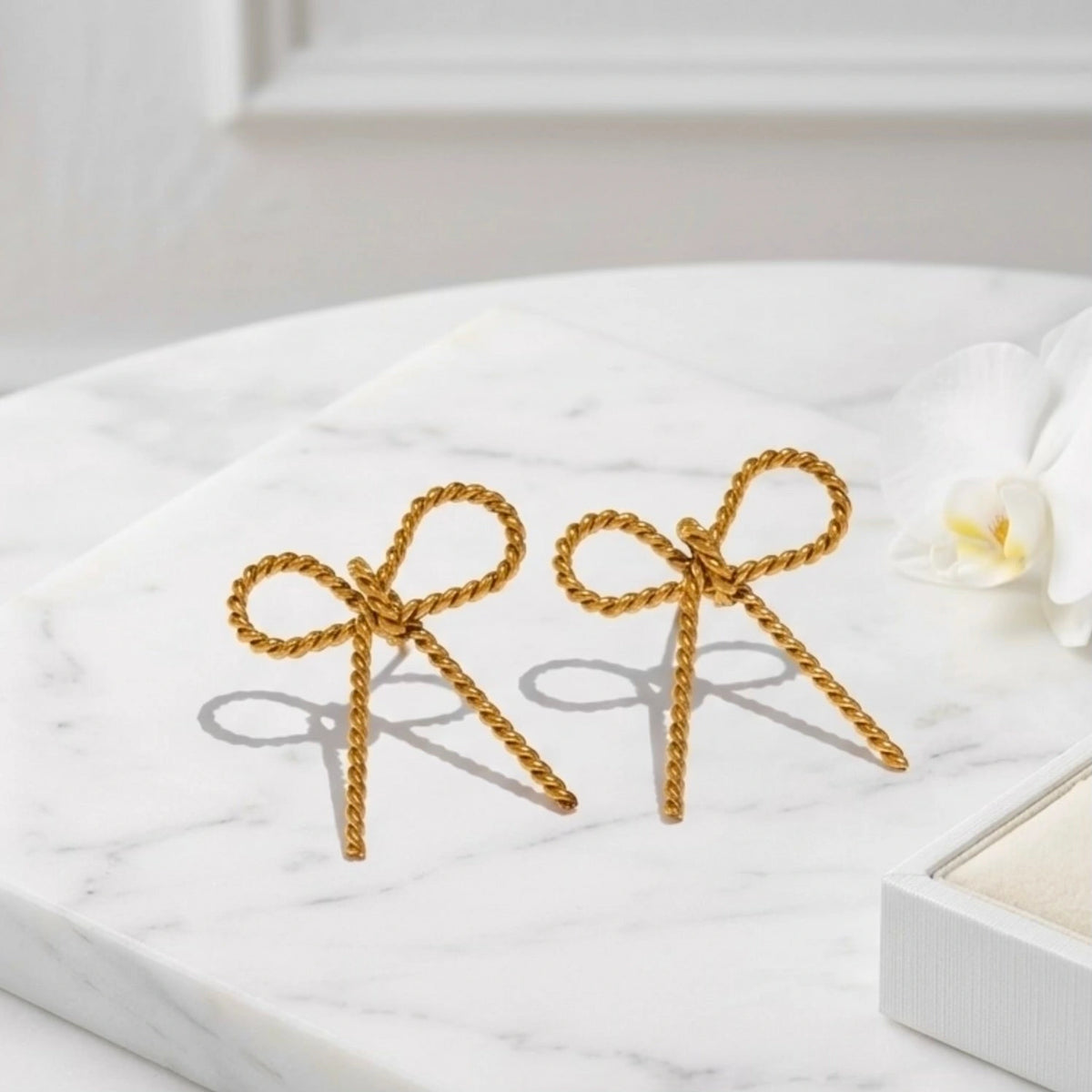 BEHI MILANO Francy Earrings — gold twisted ribbon bow earrings flat lay on white marble platform
