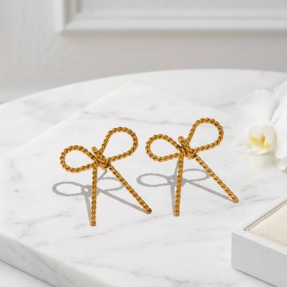 BEHI MILANO Francy Earrings — gold twisted ribbon bow earrings flat lay on white marble platform