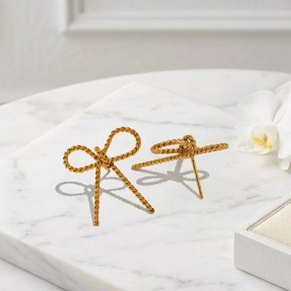 BEHI MILANO Francy Earrings — side angle view of gold twisted bow earring showing post back on marble