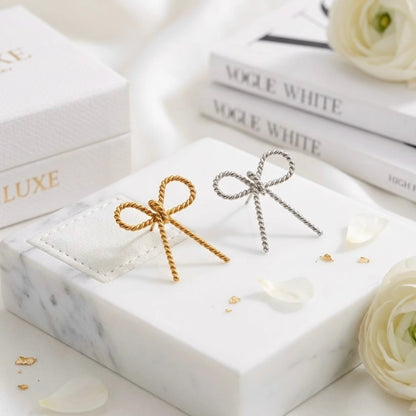 BEHI MILANO Francy Earrings — gold and silver twisted bow statement earrings displayed together on marble