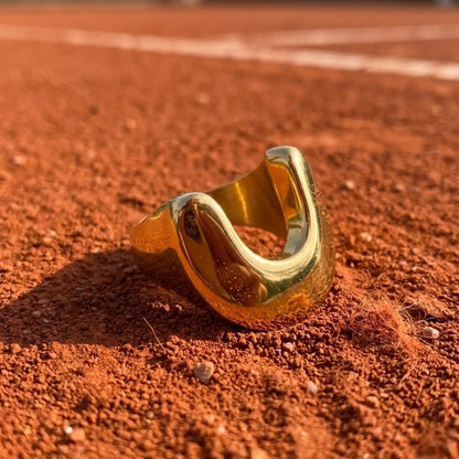 BEHI MILANO Giusy Ring — close-up of gold dipped sculptural ring resting on red clay surface