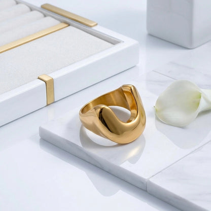 BEHI MILANO Giusy Ring — gold U-dip statement ring on white marble tray with flower petal