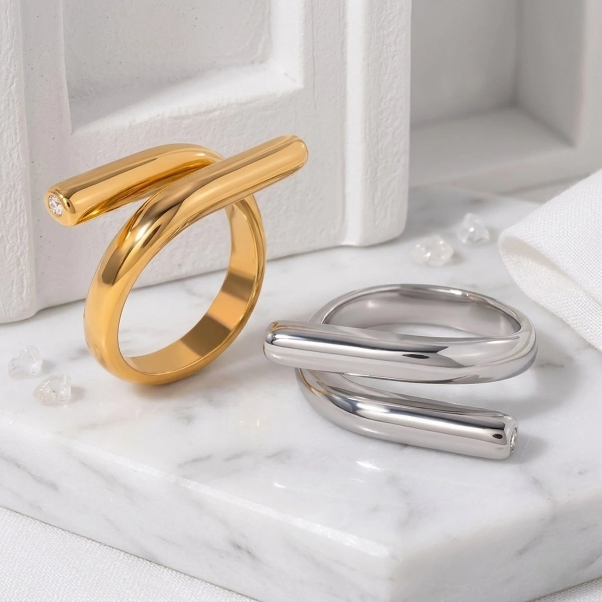 BEHI MILANO Greta Ring — gold and silver sculptural wrap statement rings on white marble