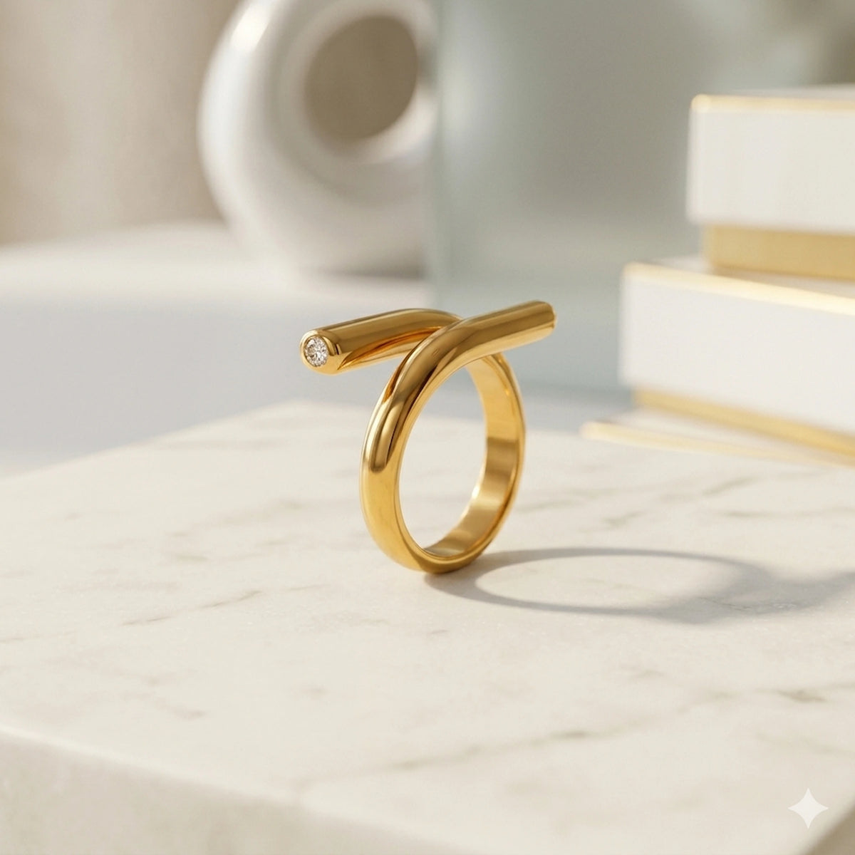 BEHI MILANO Greta Ring — gold zircon crossover ring on white marble pedestal
