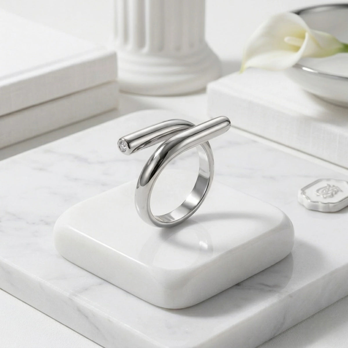 BEHI MILANO Greta Ring — silver sculptural wrap ring on white marble pedestal