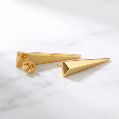 BEHI MILANO Hanika Earrings — pair of gold geometric drop studs resting flat on white marble surface