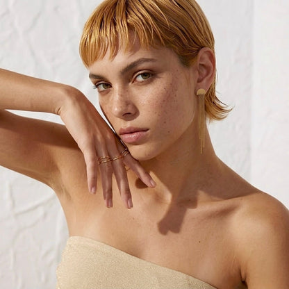 BEHI MILANO Heyley Earrings — model posing with hands near face wearing 18k gold tassel drop studs