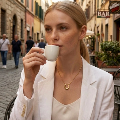 BEHI MILANO Horseshoe Necklace — model drinking espresso outdoors wearing gold horseshoe necklace