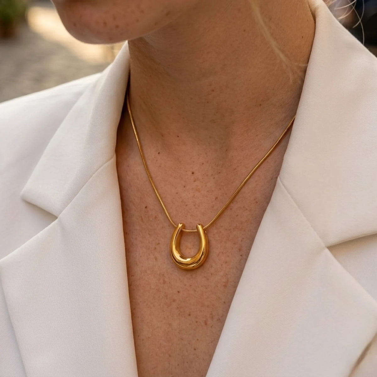 BEHI MILANO Horseshoe Necklace — model wearing 18k gold horseshoe pendant with open white blazer